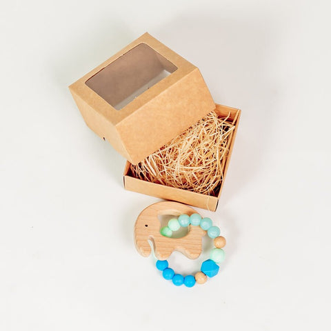2. Light blue silicone baby teether-bracelet with wooden elephant detail, shown with open brown gift box on white background