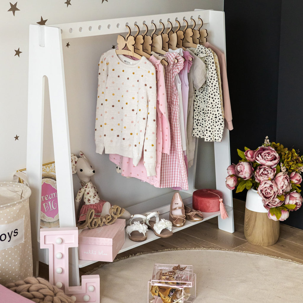 4. White toddler clothing rack with pink and patterned clothes, shoes, and toys in a cozy room setting