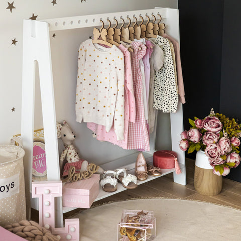 4. White toddler clothing rack with pink and patterned clothes, shoes, and toys in a cozy room setting