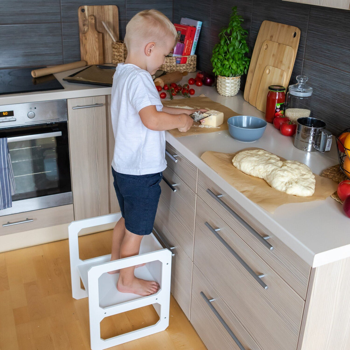 15. Boy standing on a white Montessori step stool in a kitchen preparing food