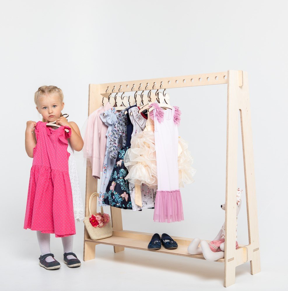 9. Natural wood toddler clothing rack with a young girl holding a pink dress in a studio setting