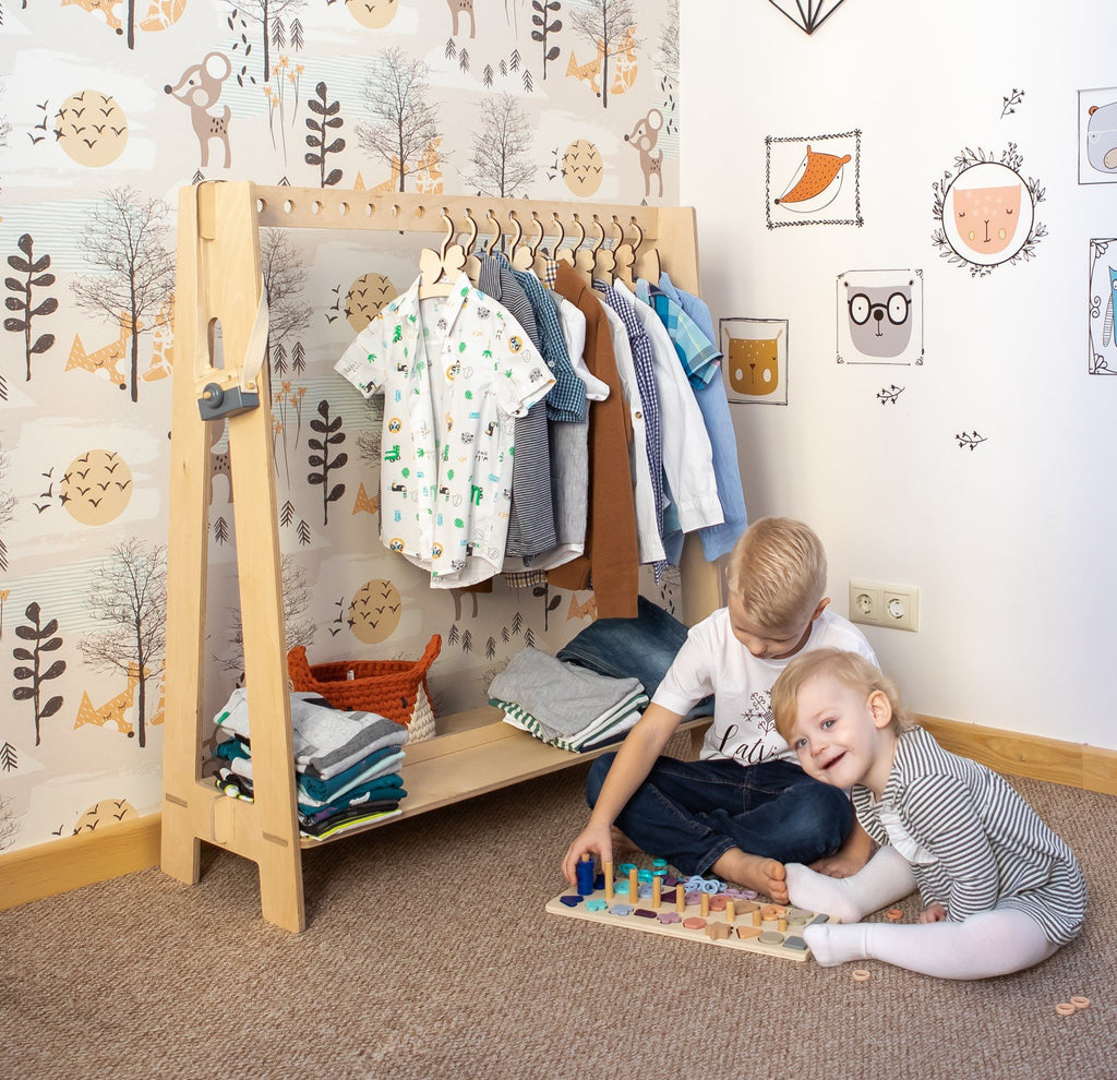 7. Natural wood toddler clothing rack with boys' clothes and two children playing in a forest-themed room