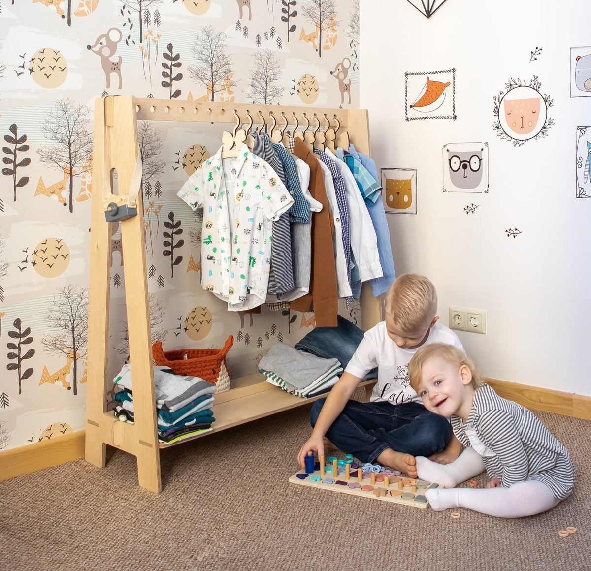 7. Natural wood toddler clothing rack with boys' clothes and two children playing in a forest-themed room
