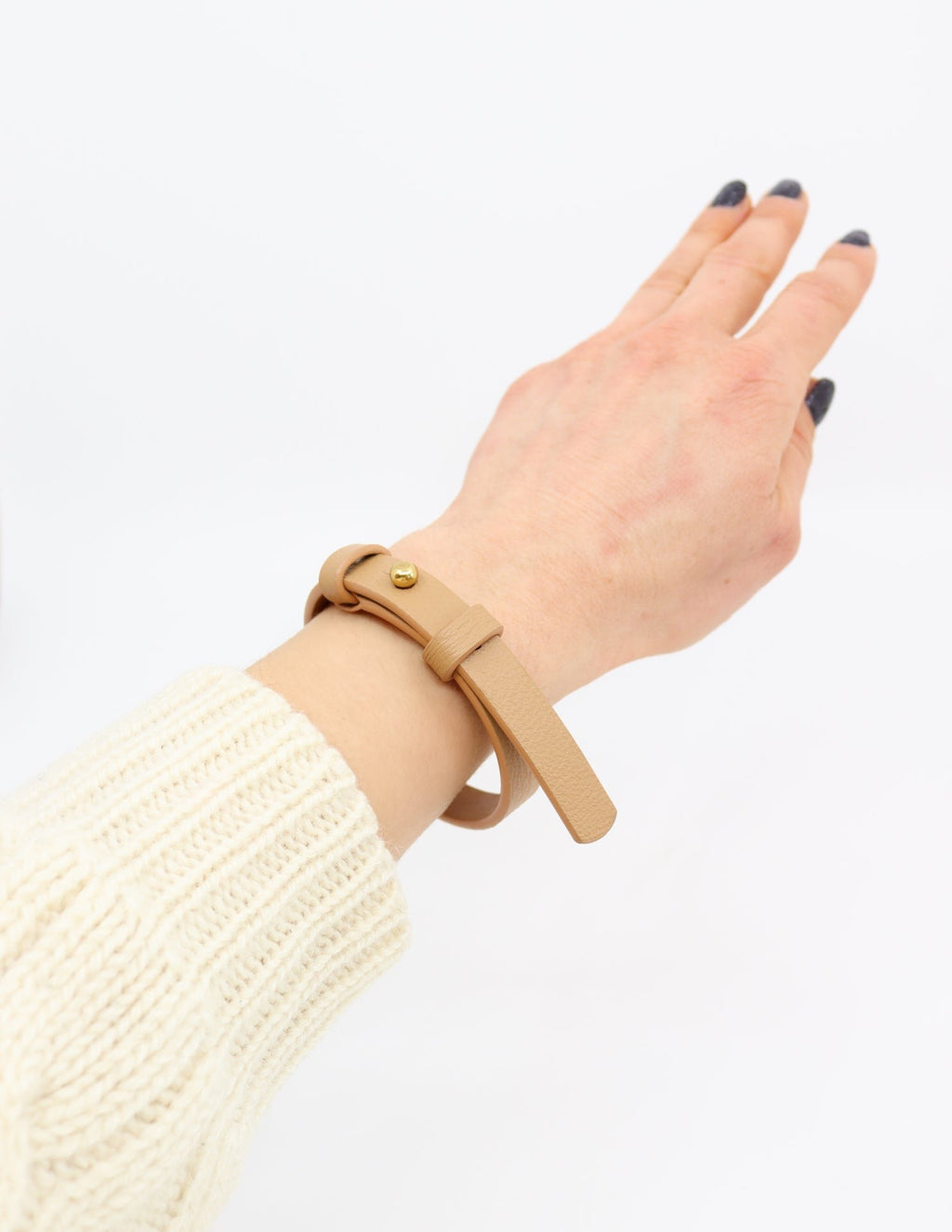 1. Women's hand wearing Tairi Roosve leather bracelet in desert tan with brass fastener, shown in lifestyle setting