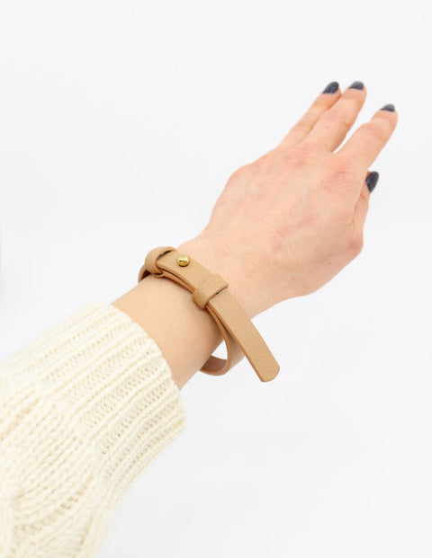 1. Women's hand wearing Tairi Roosve leather bracelet in desert tan with brass fastener, shown in lifestyle setting