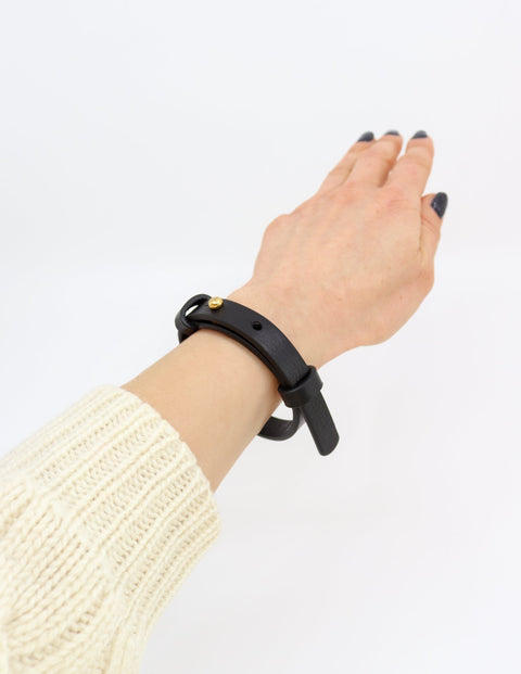 3. Black leather bracelet with brass fastener worn by a woman, shown on wrist
