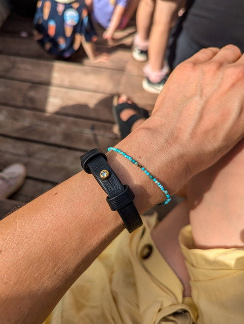 5. Black leather bracelet with brass fastener worn outdoors, paired with a blue beaded bracelet