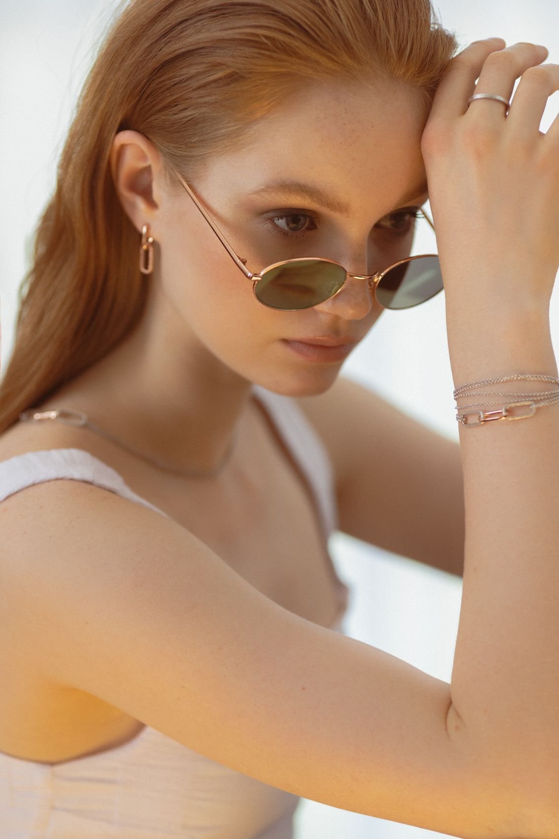 1. Woman wearing MyaMoon Metropolitan Earrings in rose gold, styled with sunglasses and a white top, showcasing elegant city vibes