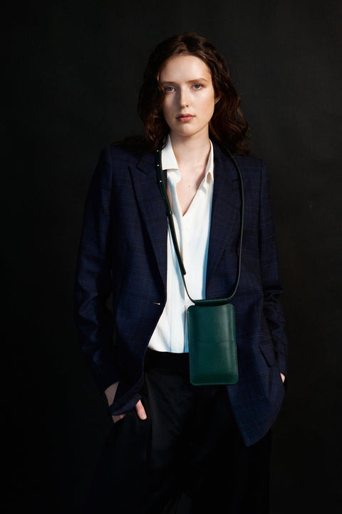 1. Woman wearing Tairi Roosve leather phone bag in forest green, styled with a blazer, showcasing crossbody design