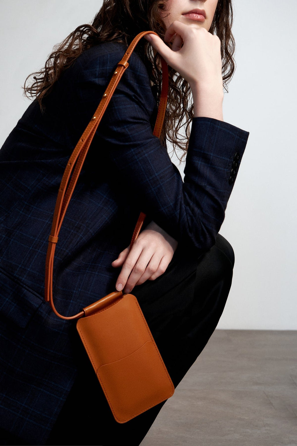2. Woman wearing Tairi Roosve tan leather phone bag crossbody, showcasing adjustable strap in lifestyle setting