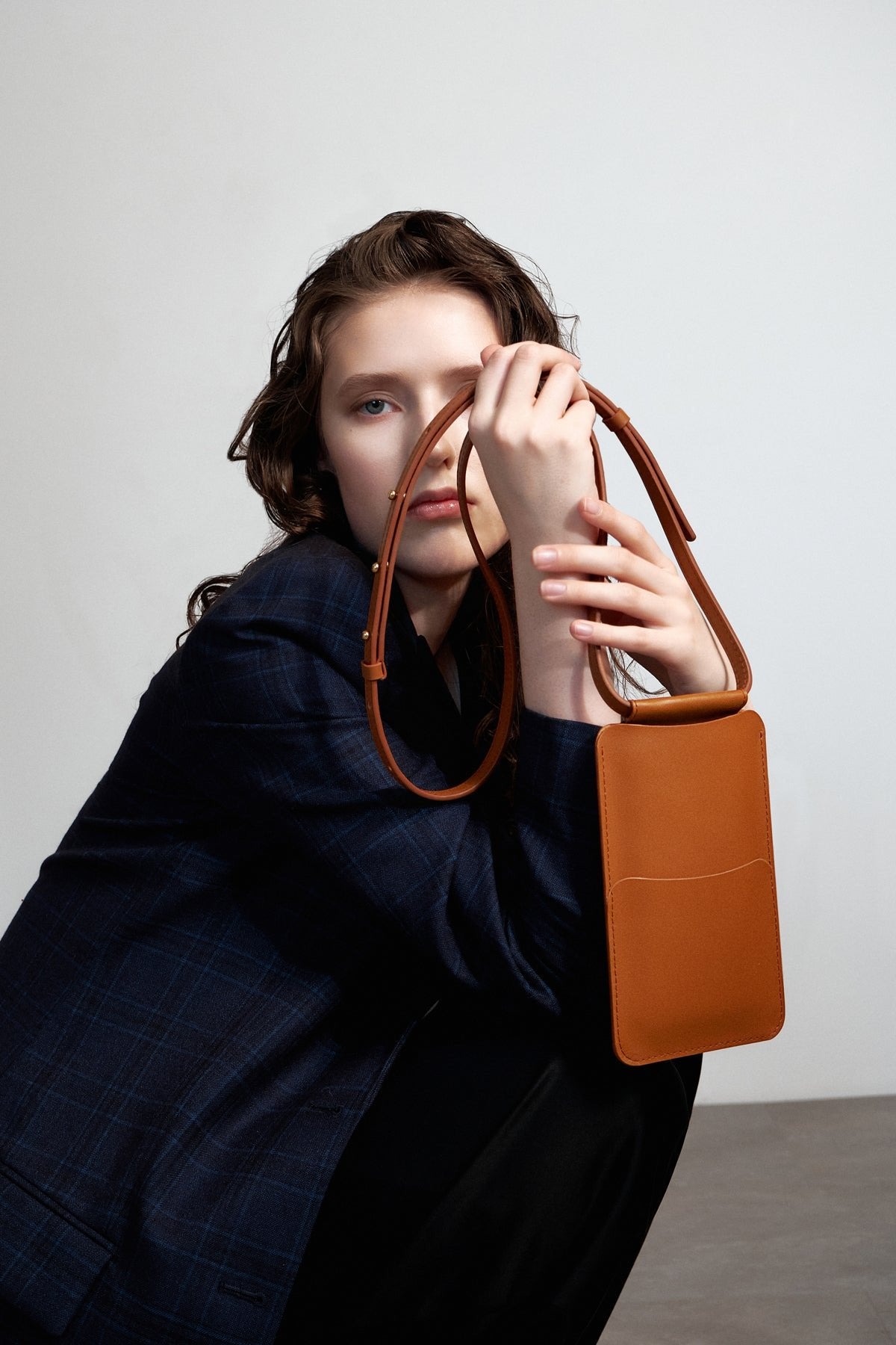 1. Woman holding Tairi Roosve tan leather phone bag with adjustable strap, styled in a lifestyle setting