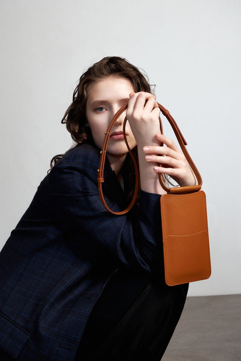 1. Woman holding Tairi Roosve tan leather phone bag with adjustable strap, styled in a lifestyle setting