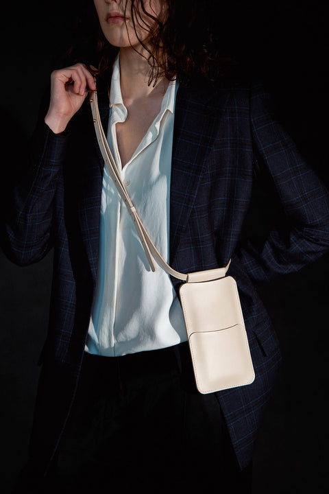 1. Women's beige leather phone bag by Tairi Roosve worn crossbody, shown in lifestyle setting