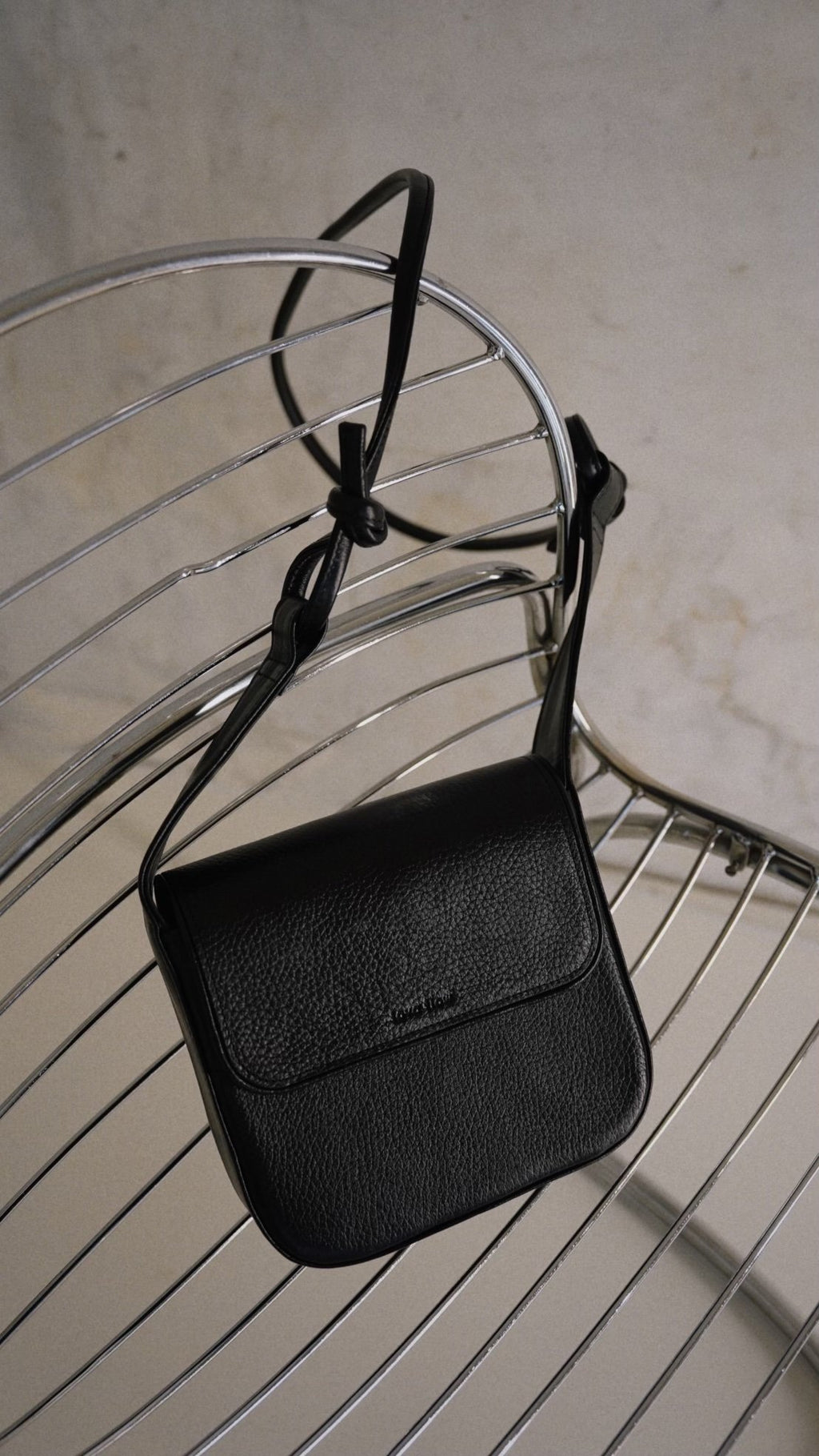 7. Black MUSA crossbody bag by Lava Flow, displayed on metal chair, close-up view