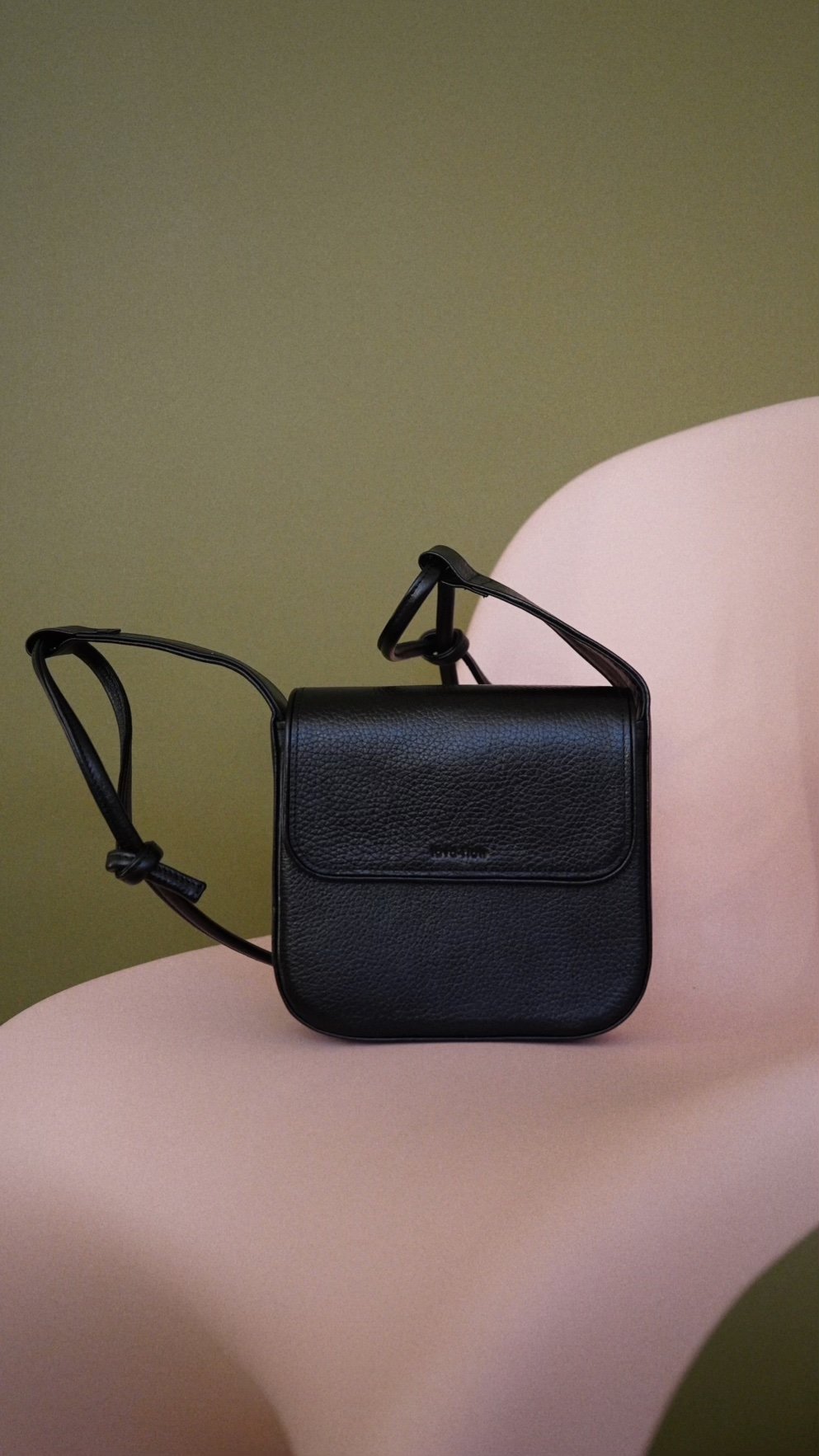 6. Black MUSA crossbody bag by Lava Flow, displayed on pink chair, close-up view