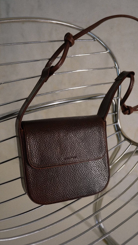 4. Close-up of brown MUSA crossbody bag by Lava Flow on metal chair, featuring natural leather and adjustable strap