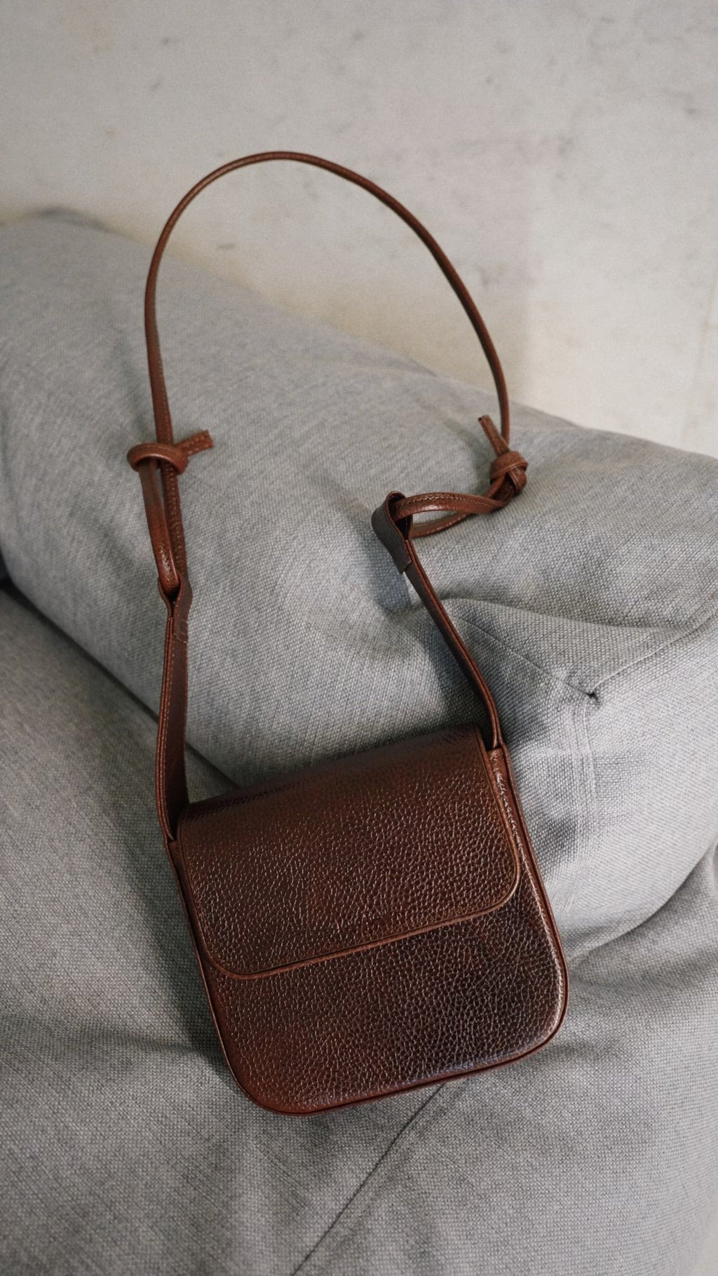 3. Studio shot of brown MUSA crossbody bag by Lava Flow on grey sofa, showing Italian vegetable-tanned leather texture