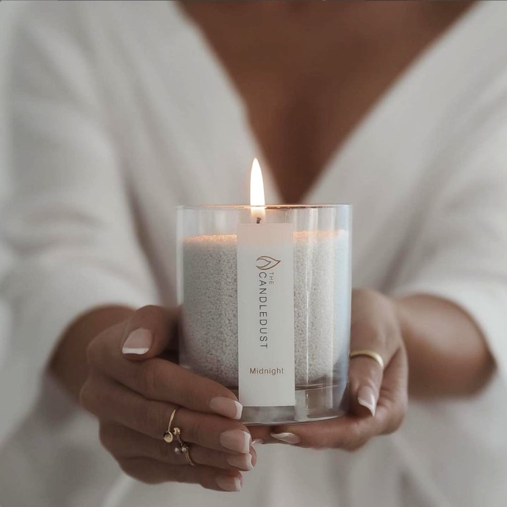 1. Woman holding lit Candledust Midnight powdered candle in glass, showcasing elegant design and warm glow