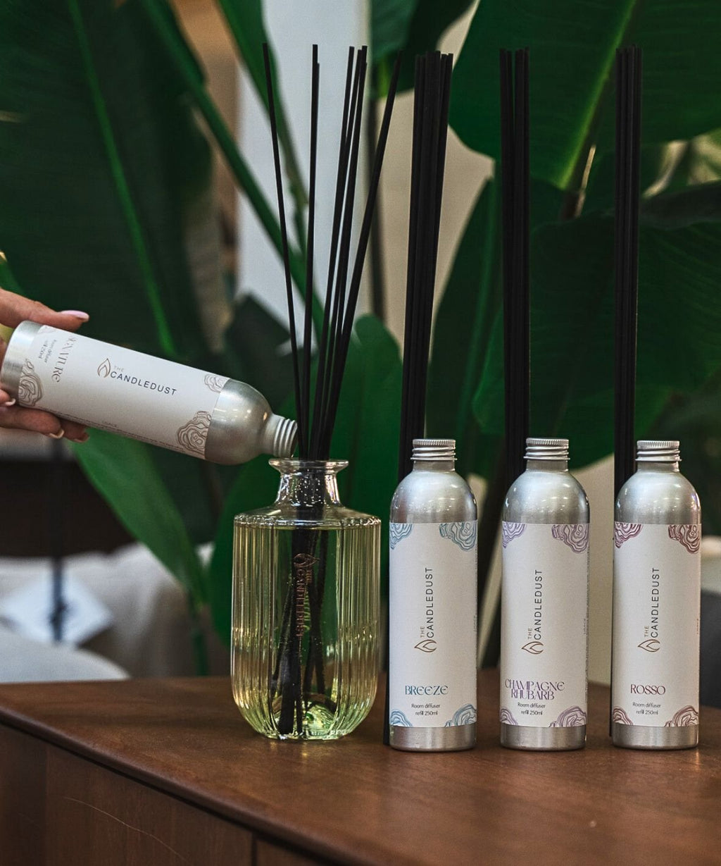 2. Candledust Champagne Rhubarb diffuser refill being poured into a glass diffuser with other scents displayed