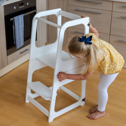 1. Young girl adjusting white transformable kitchen tower in modern kitchen setting