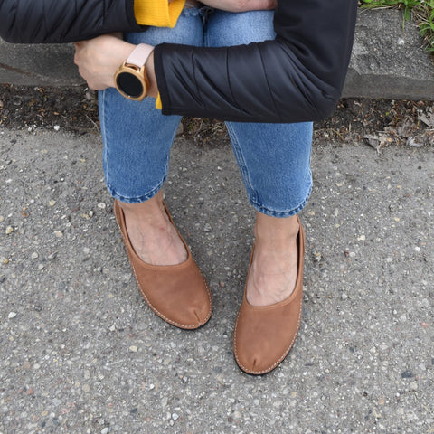 2. Woman sitting on a bench wearing Omaking Kuutsid brown leather shoes with jeans