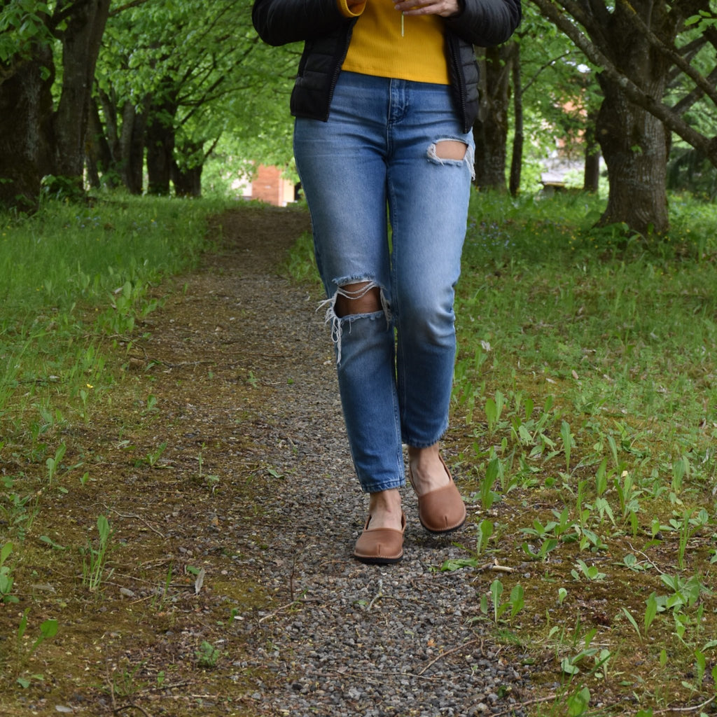 1. Woman walking on a forest path wearing Omaking Kuutsid brown leather shoes with jeans