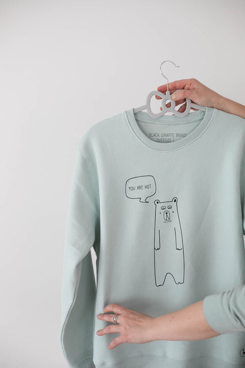 2. Sage Green oversized sweatshirt by Black Giraffe Brand with 'You are hot' bear graphic, held by hand