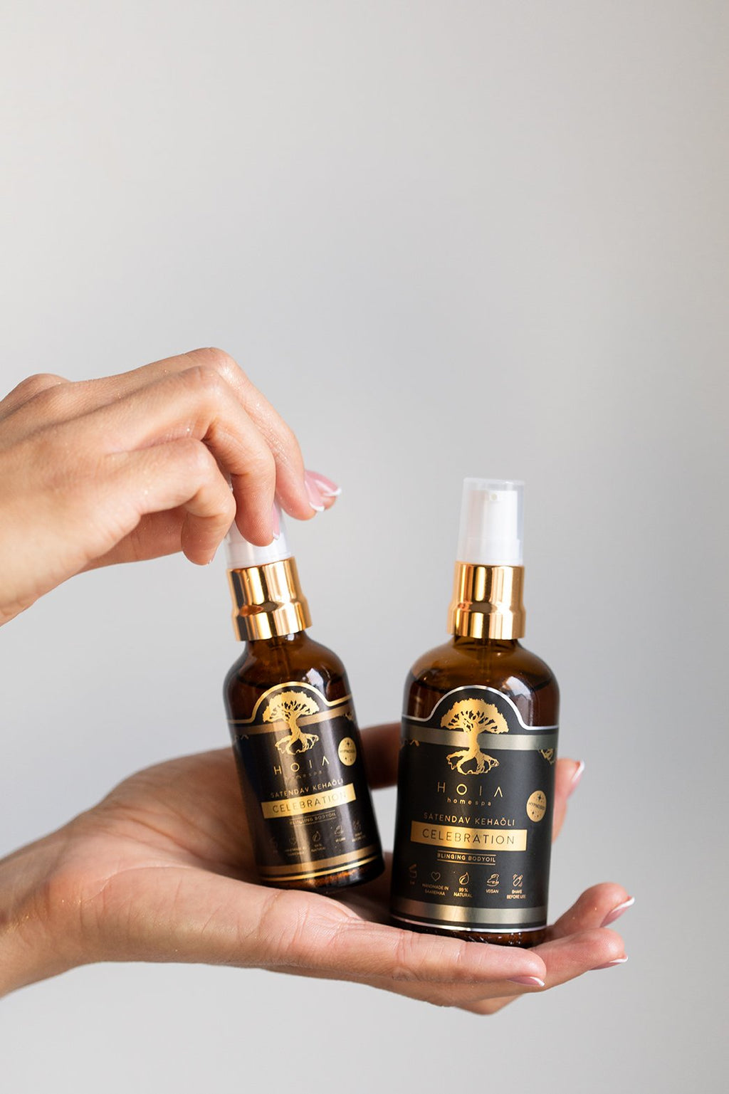 3. Two bottles of HOIA homespa Shimmering Body Oil held in hand, studio setting