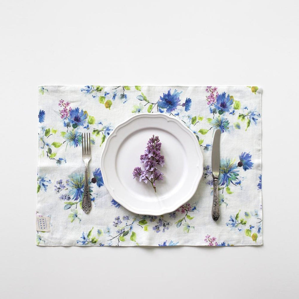 2. White floral linen placemat with a purple flower on a white plate, set with a fork and knife
