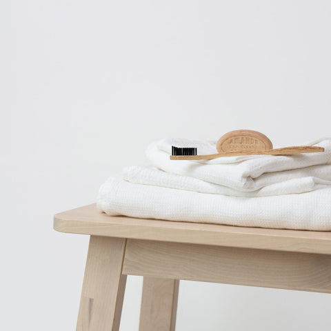 5. Stack of white waffle linen towels on wooden bench with wooden brush, showcasing soft texture and elegant bathroom accessory