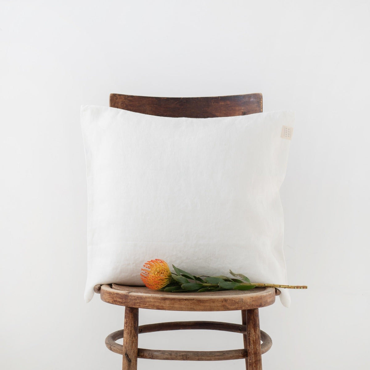 7. White Linen Tales cushion cover on a wooden chair with an orange flower