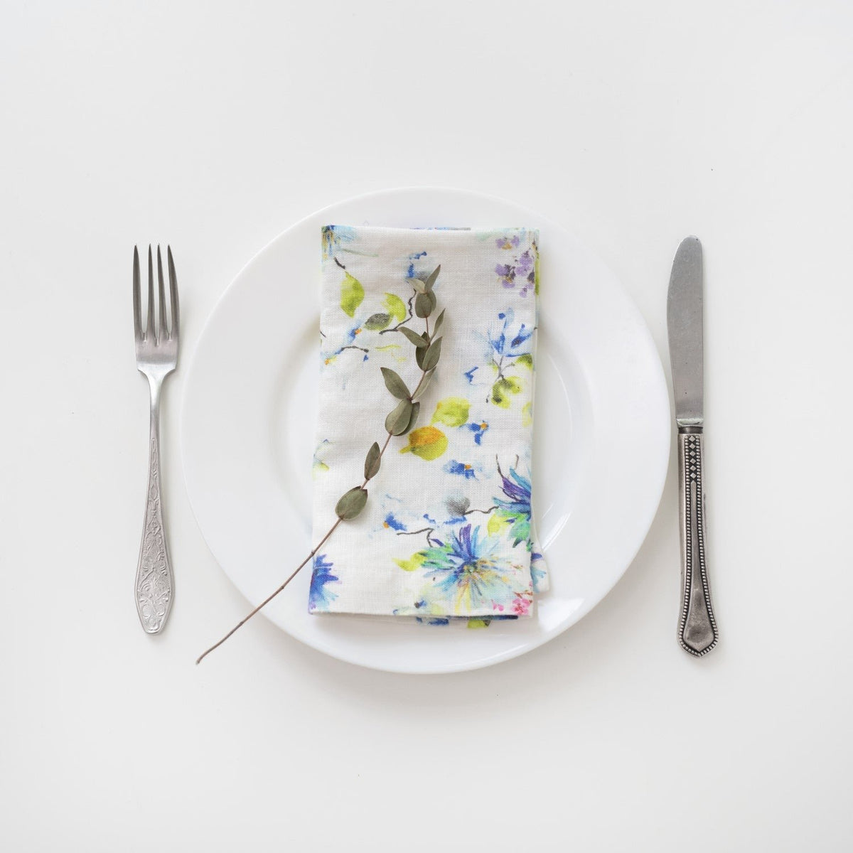 12. Floral linen napkin on a white plate with a decorative twig, accompanied by fork and knife