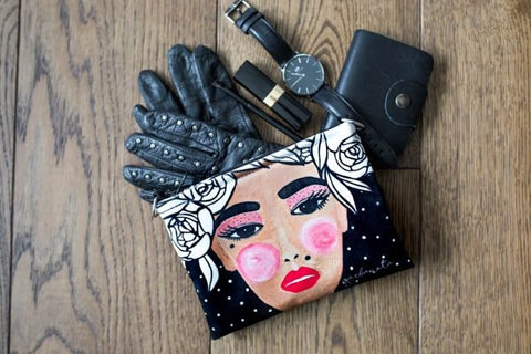 4. Garbanota YOKO makeup bag in black with face print, styled with gloves, watch, and wallet on wooden surface