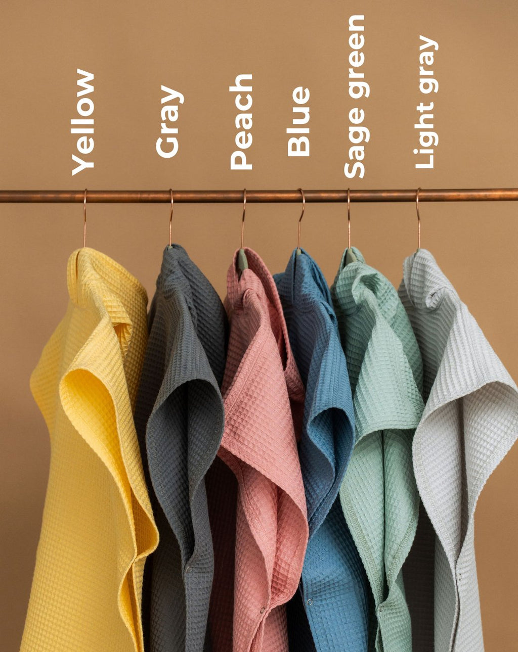 7. Hanging waffle fabric ponchos in yellow, gray, peach, blue, sage green, and light gray with labels