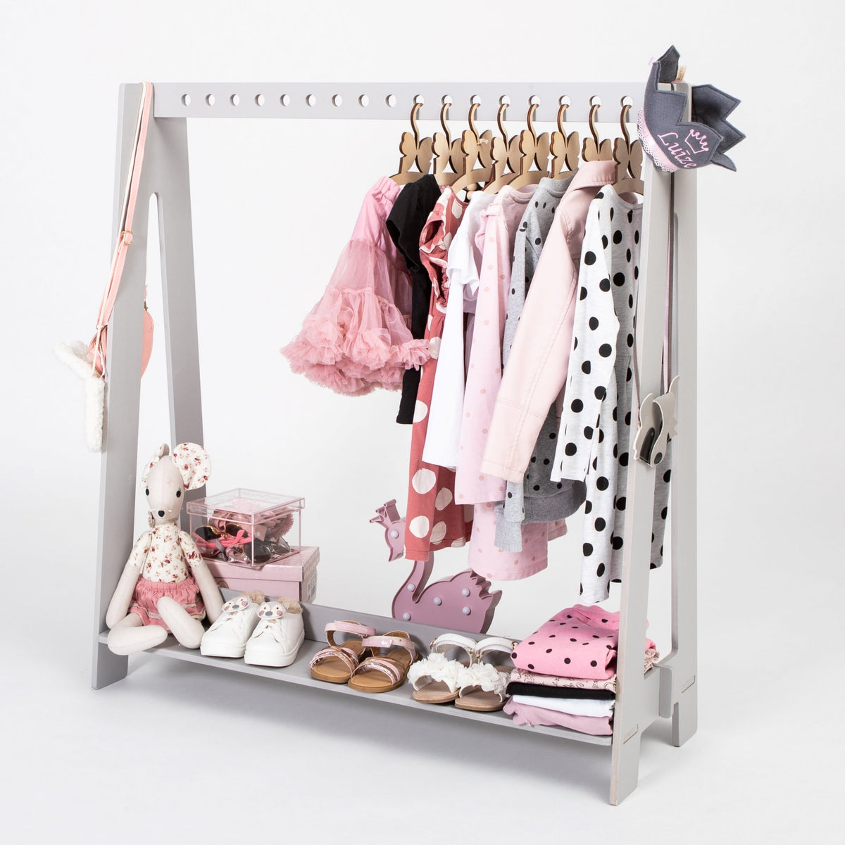 1. Grey toddler clothing rack with various pink and polka dot outfits, shoes, and toys displayed in a child's room