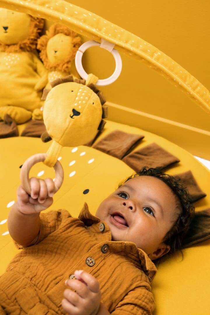 3. Close-up of baby reaching for lion-shaped toy on yellow activity play mat with arches, highlighting sensory elements
