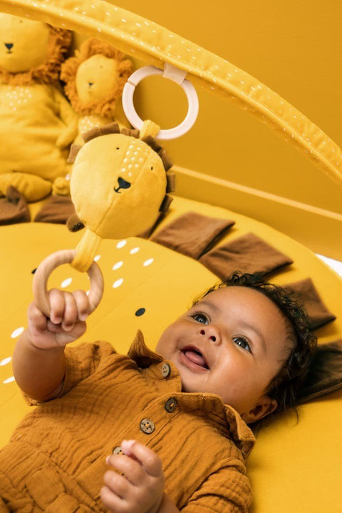 3. Close-up of baby reaching for lion-shaped toy on yellow activity play mat with arches, highlighting sensory elements