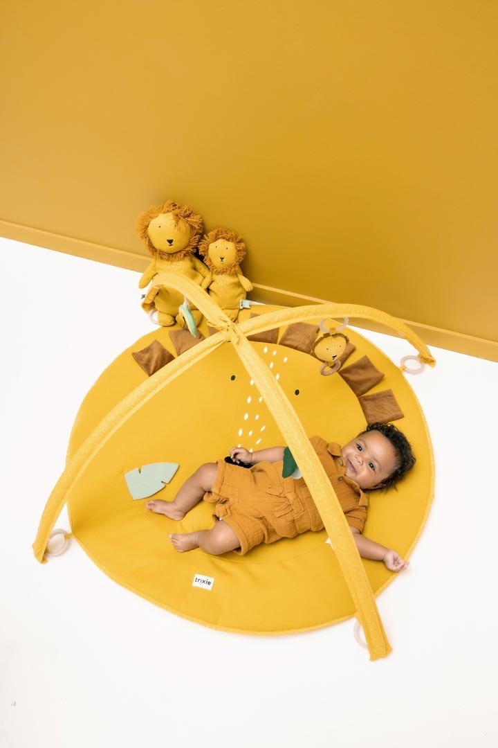 1. Baby lying on yellow lion-themed activity play mat with arches and toys, surrounded by plush lion toys, in a nursery setting
