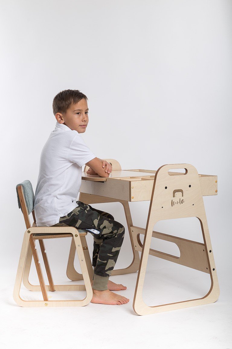 12. Boy sitting on mint green children's chair at wooden desk on white background