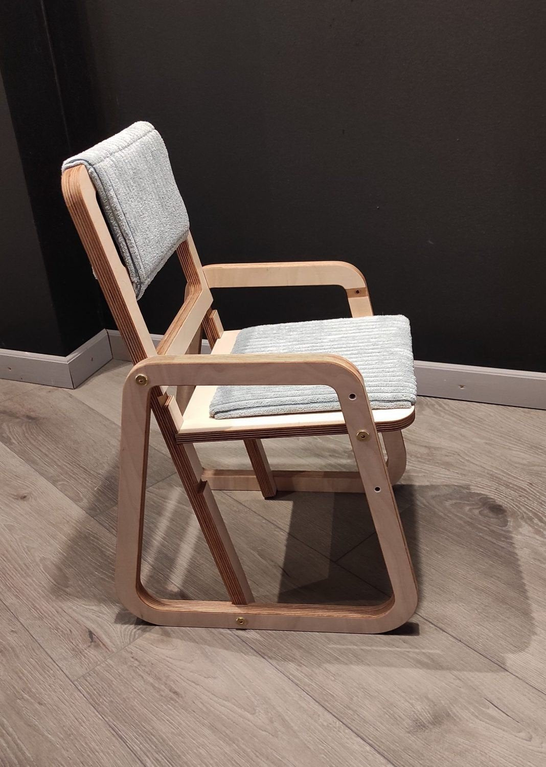 2. Side view of mint green children's chair with natural wood frame against dark wall