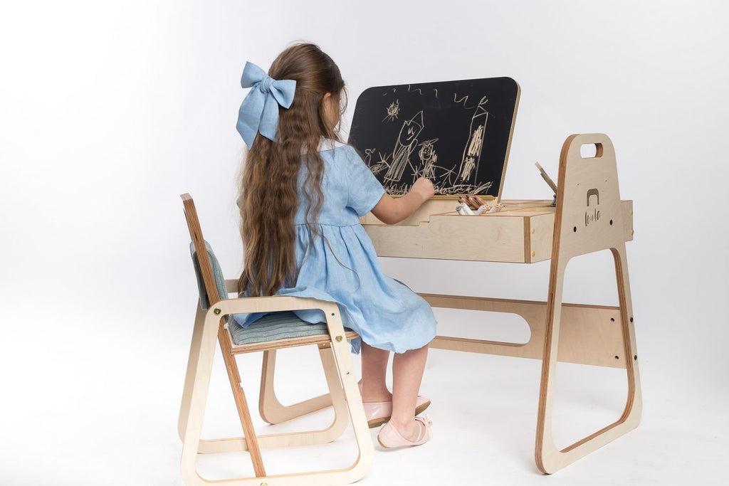 13. Girl drawing at desk while sitting on mint green children's chair on white background