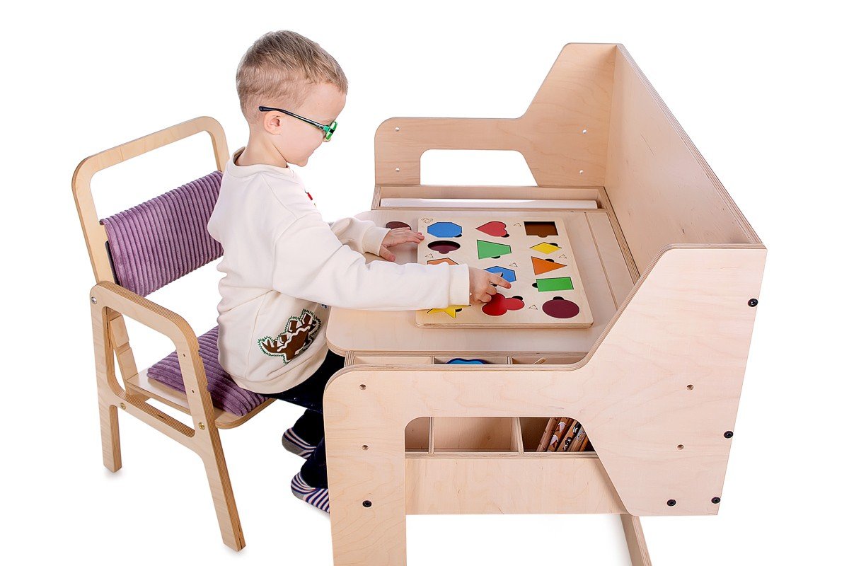 1. Child sitting on adjustable children's chair in cannon pink, playing at a wooden desk, in a studio setting