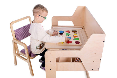 1. Child sitting on adjustable children's chair in cannon pink, playing at a wooden desk, in a studio setting