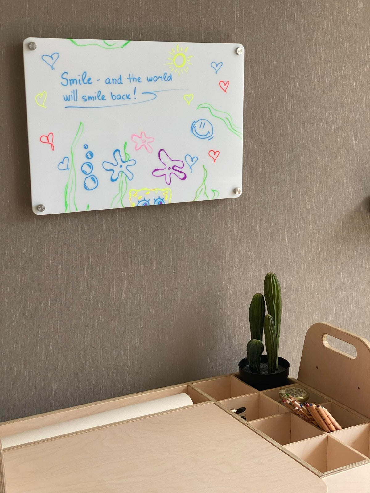 10. LUULA acrylic whiteboard mounted on wall with colorful drawings and desk below