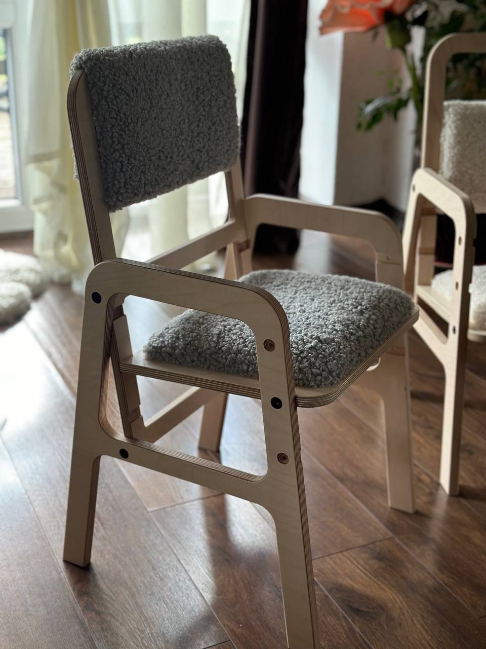 2. Adjustable children's chair in natural Baltic birch with grey padded seat and backrest, shown in a cozy room setting on wooden floor