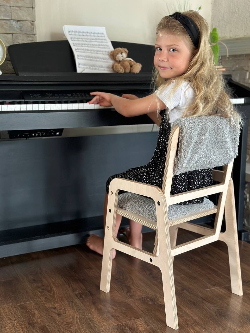 1. Girl playing piano while seated on an adjustable Luula children's chair with grey padding, in a home setting