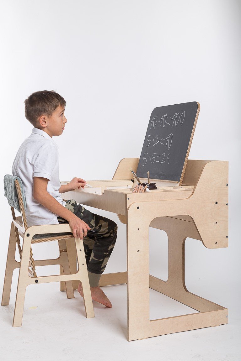 1. Boy sitting on mint green adjustable children's chair at a wooden desk with chalkboard, wearing a white shirt and camo pants