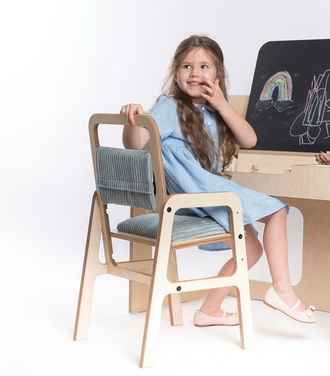 1. Girl sitting on mint green adjustable children's chair at a desk with chalkboard, wearing a blue dress, smiling