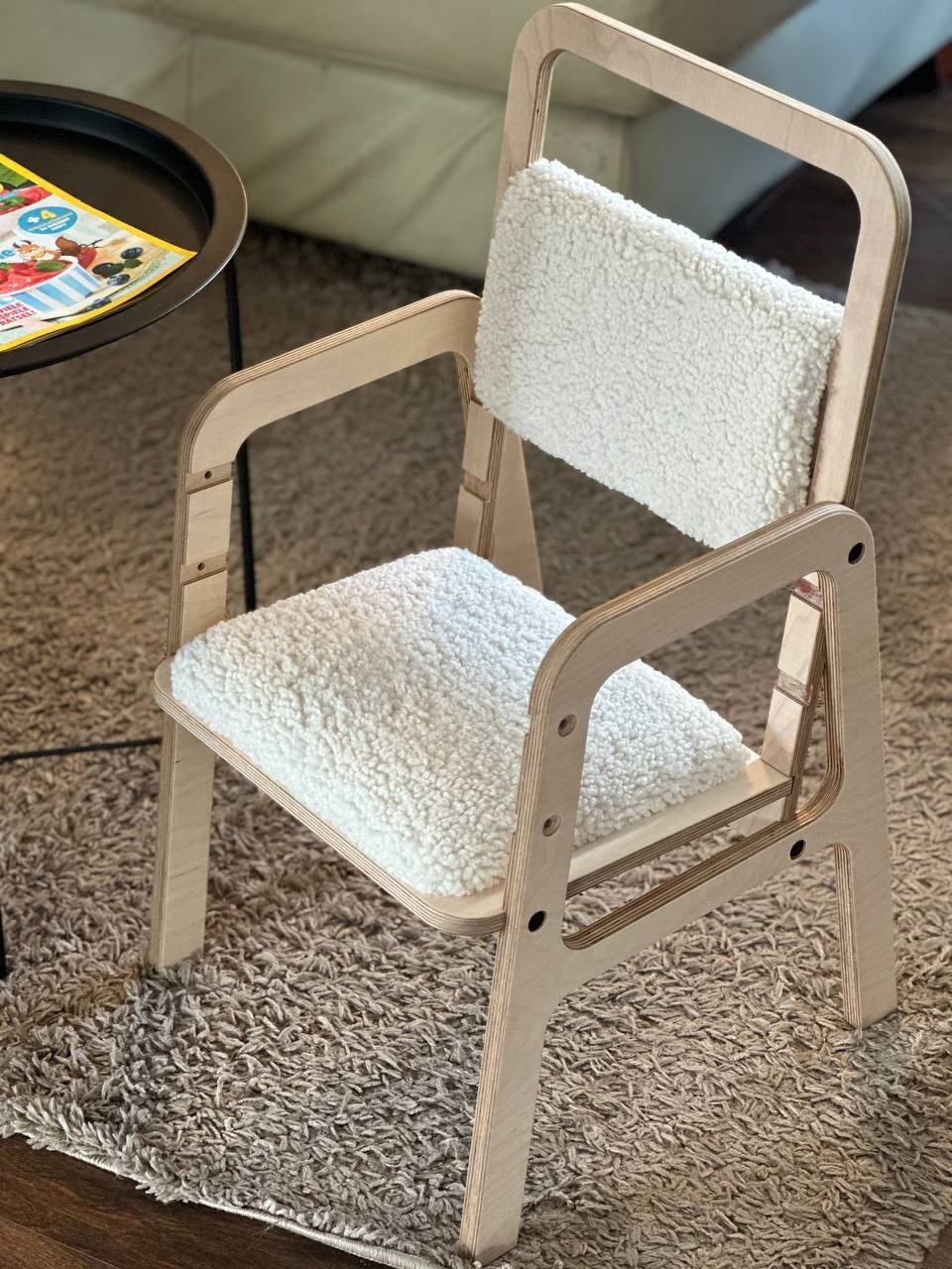 6. Luula adjustable children's chair in natural wood with vanilla lamb padding, placed on a textured rug next to a coffee table