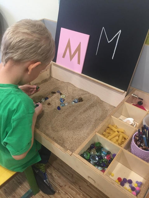 4. Boy playing with sand and colorful objects on a Montessori table, emphasizing sensory play and learning.